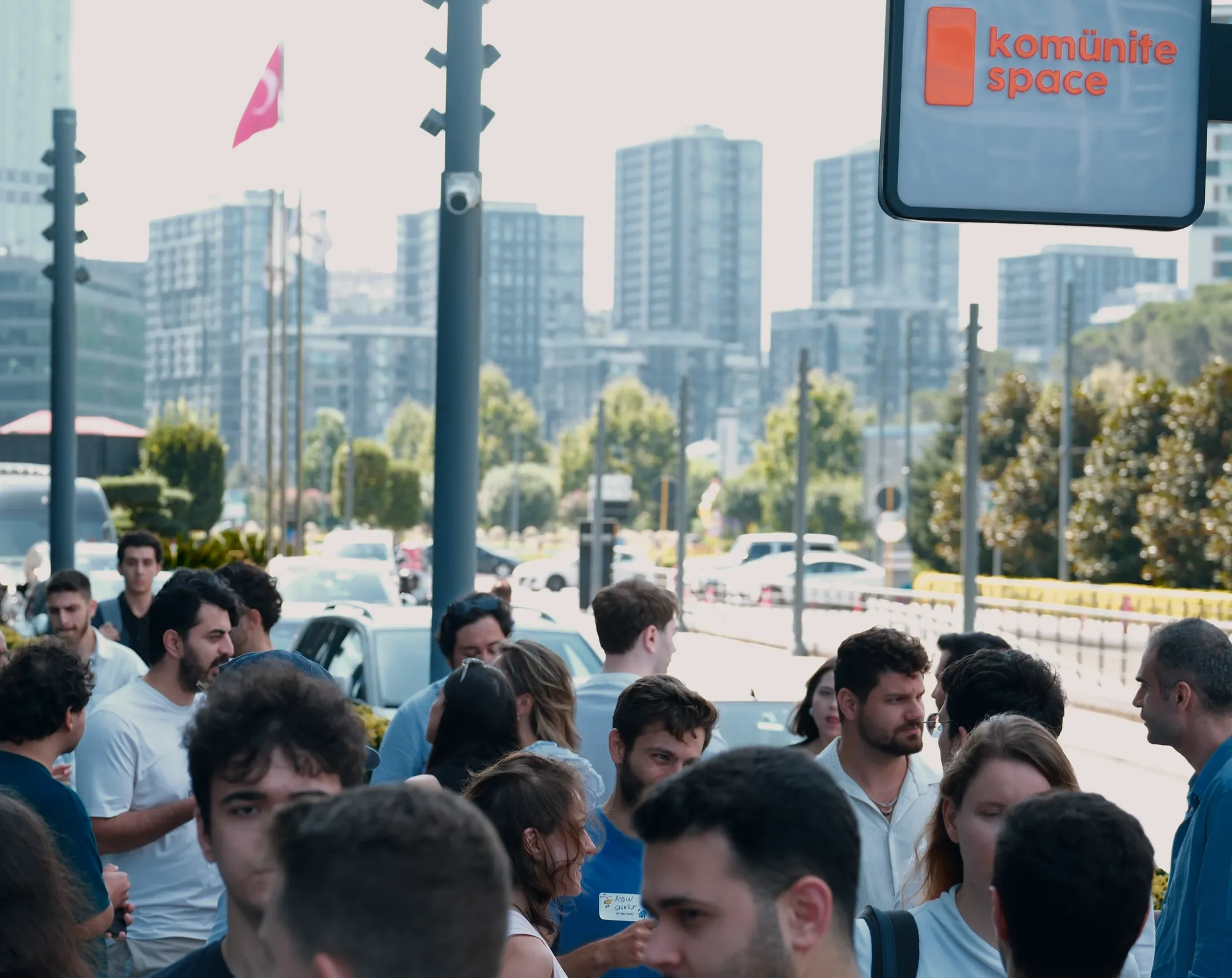 Kapının önü: Komünite Space tabelasının altında sohbet eden kalabalık, arkada Vadistanbul’un binaları.